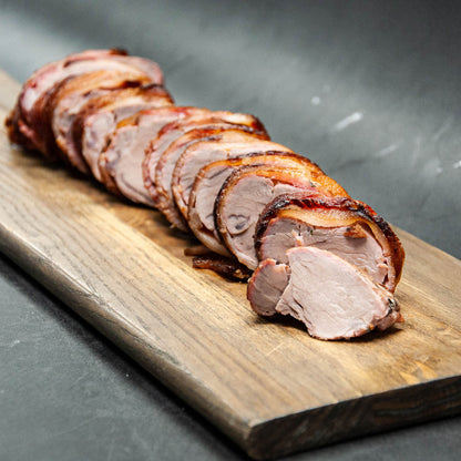 Sliced roasted pork on a wooden cutting board with a dark background