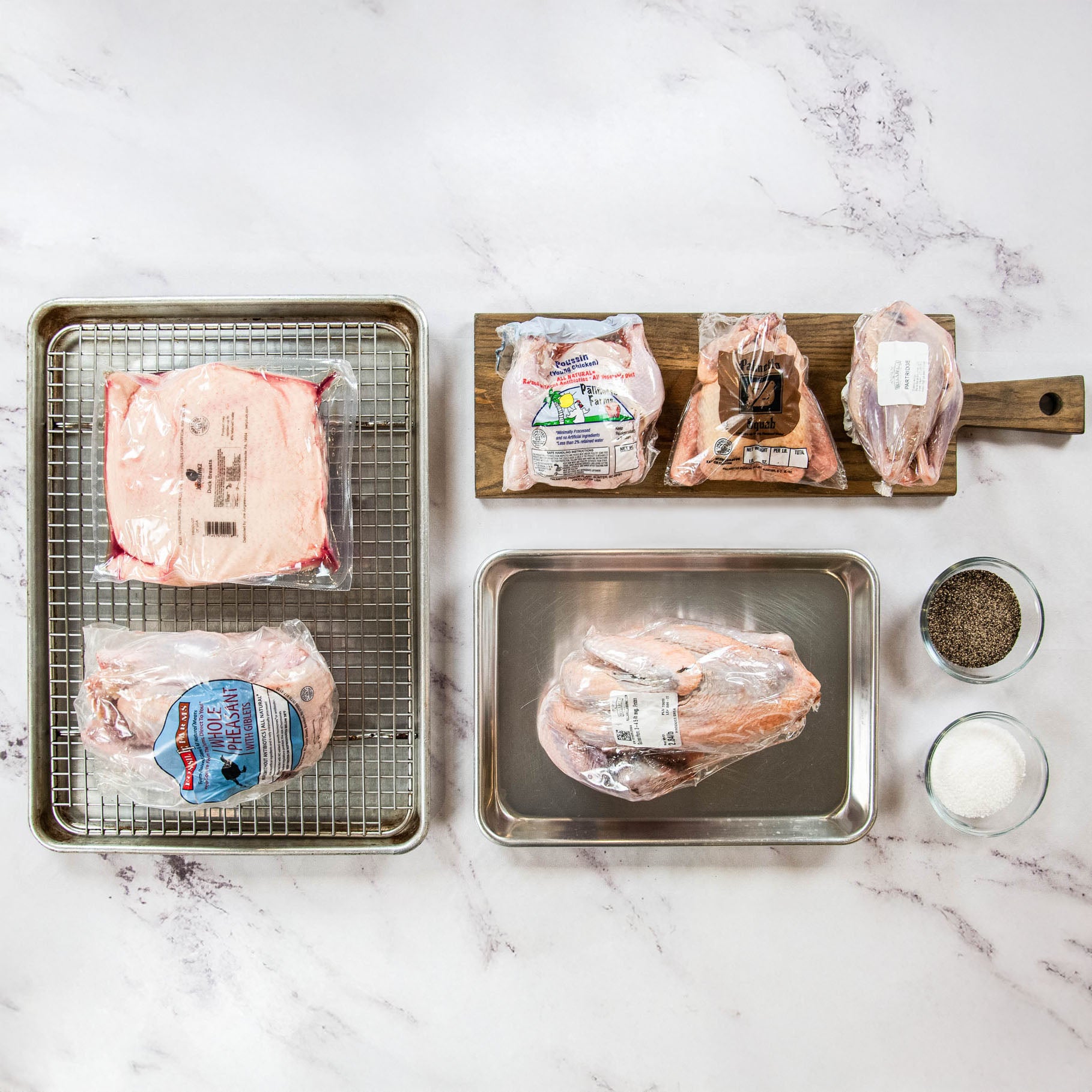 Raw chicken breasts on a marble countertop with a metal rack and small containers of spices.
