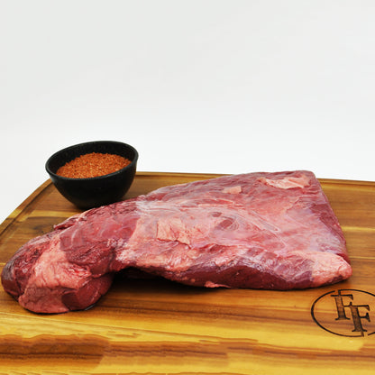 Raw beef brisket on a wooden cutting board with a small bowl of spices.