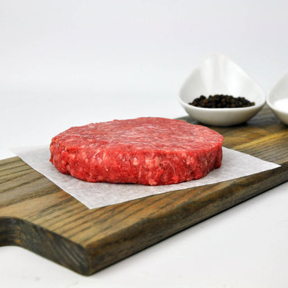 Raw hamburger patty on a wooden cutting board with a white background
