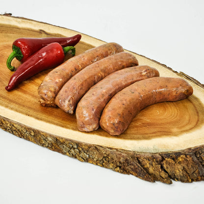 Raw sausages on a wooden cutting board with red peppers