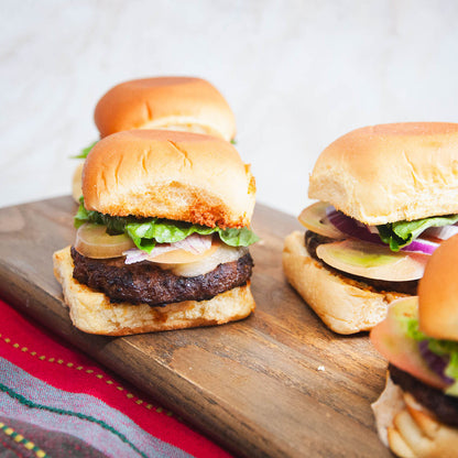 Three sliders with beef patties, lettuce, and onions on a wooden board.