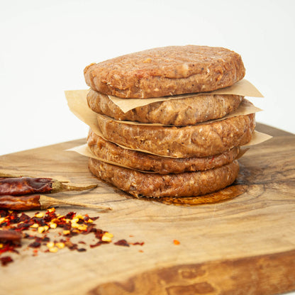 Stack of raw burger patties on a wooden cutting board with red pepper flakes.