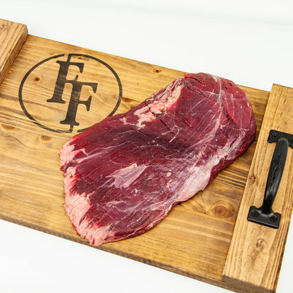 Raw steak on a wooden cutting board with a brand logo.