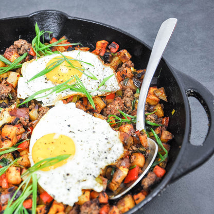 Skillet with breakfast hash and fried eggs on a gray surface