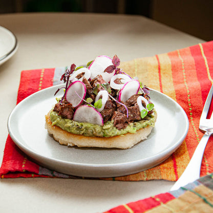 Plated dish with guacamole, meat, and radishes on a colorful napkin