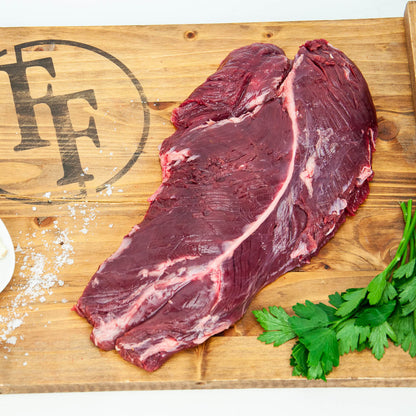 Two raw steaks on a wooden cutting board with herbs and salt.