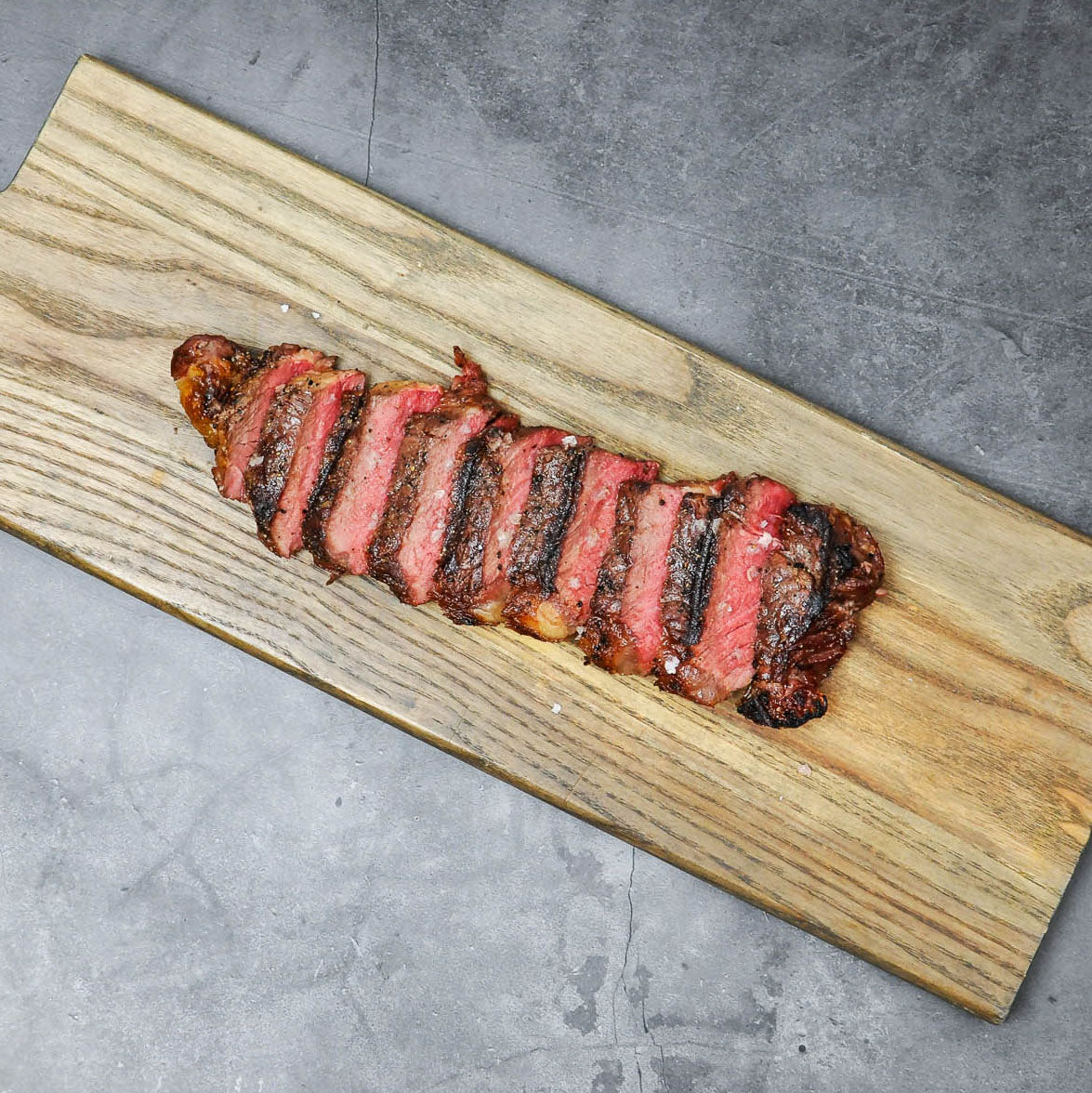 Sliced steak on a wooden board with a gray concrete background