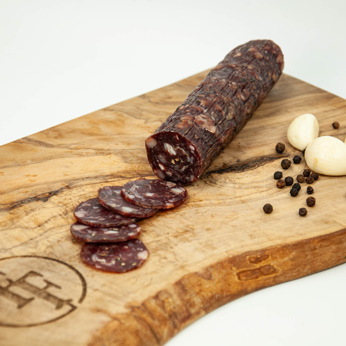 Salami with slices on a wooden cutting board with garlic and peppercorns.