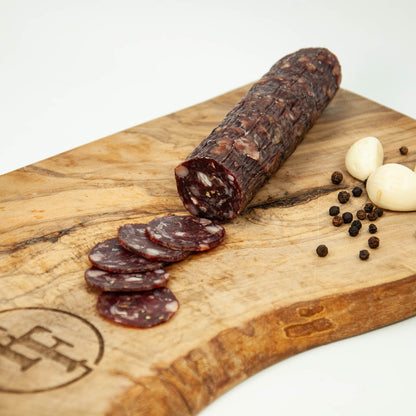Salami with slices on a wooden cutting board with garlic and peppercorns.