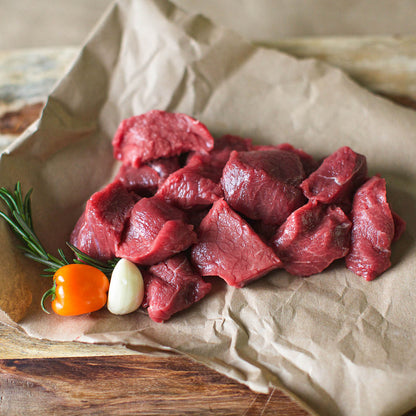 Raw beef pieces on brown paper with a pepper and garlic on a wooden surface