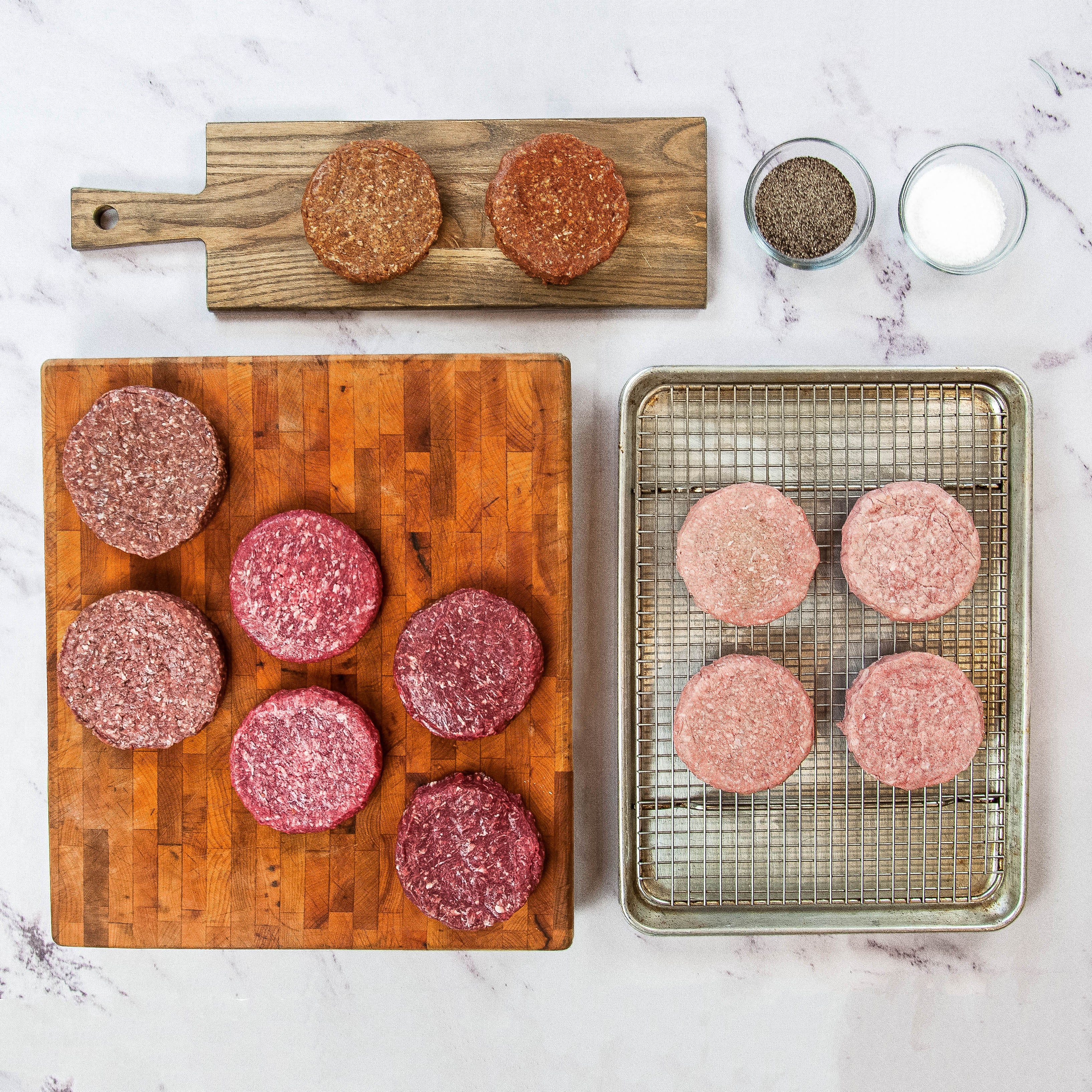 Raw hamburger patties on a wooden cutting board and metal tray.