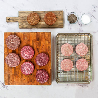 Raw hamburger patties on a wooden cutting board and metal tray.