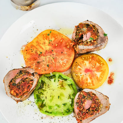 Stuffed meat rolls with colorful tomatoes on a white plate