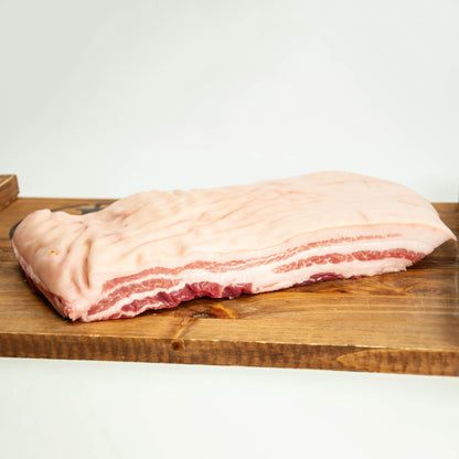 Raw pork belly on a wooden cutting board with a white background
