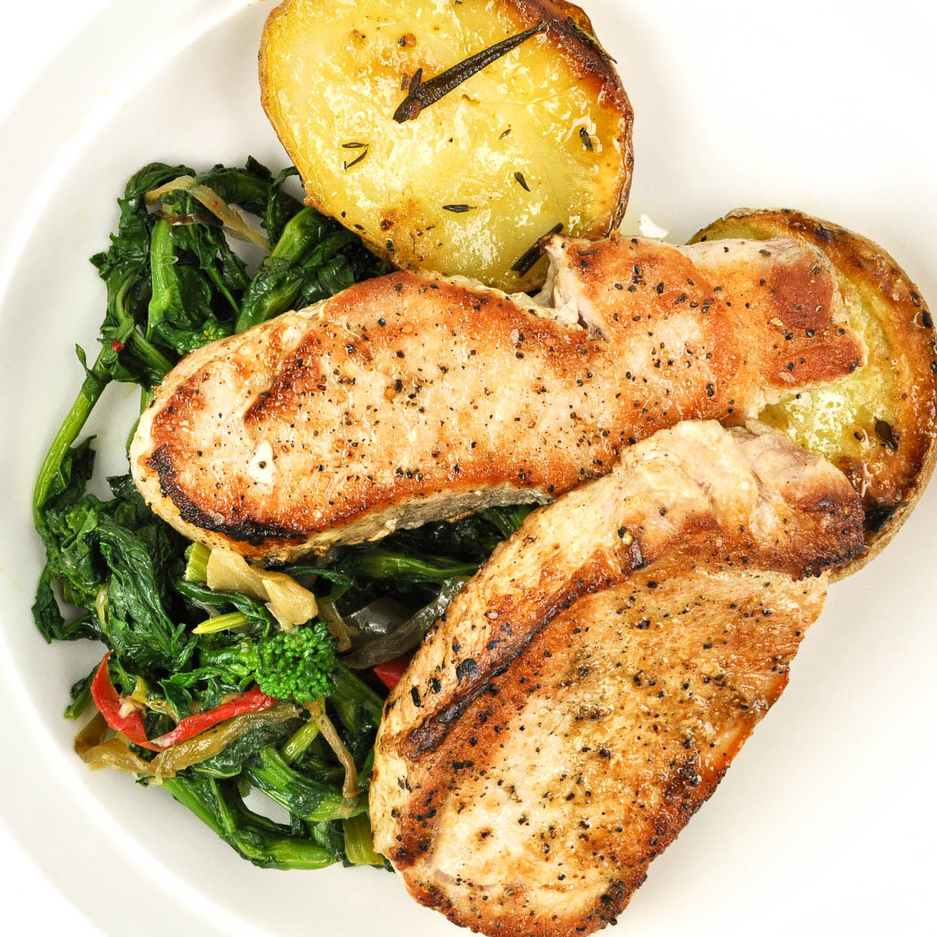 Plated dish with pork chops, roasted potatoes, and sautéed greens on a white plate.