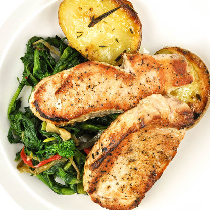 Plated dish with pork chops, roasted potatoes, and sautéed greens on a white plate.
