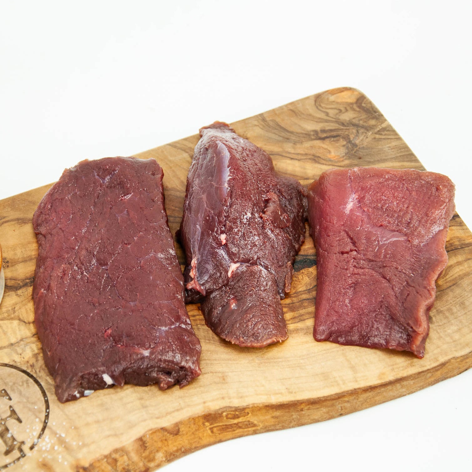Three pieces of raw beef on a wooden cutting board with a white background
