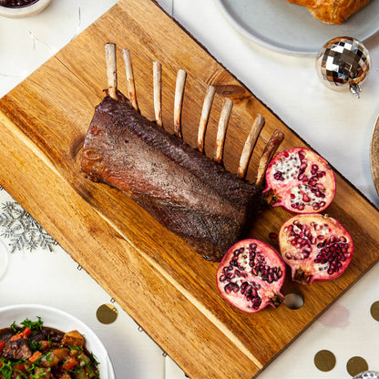 Roasted rack of lamb with pomegranate on a wooden cutting board