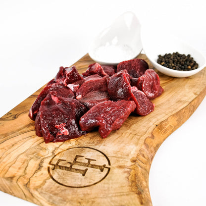 Raw beef chunks on a wooden cutting board with a logo, surrounded by small bowls of spices.