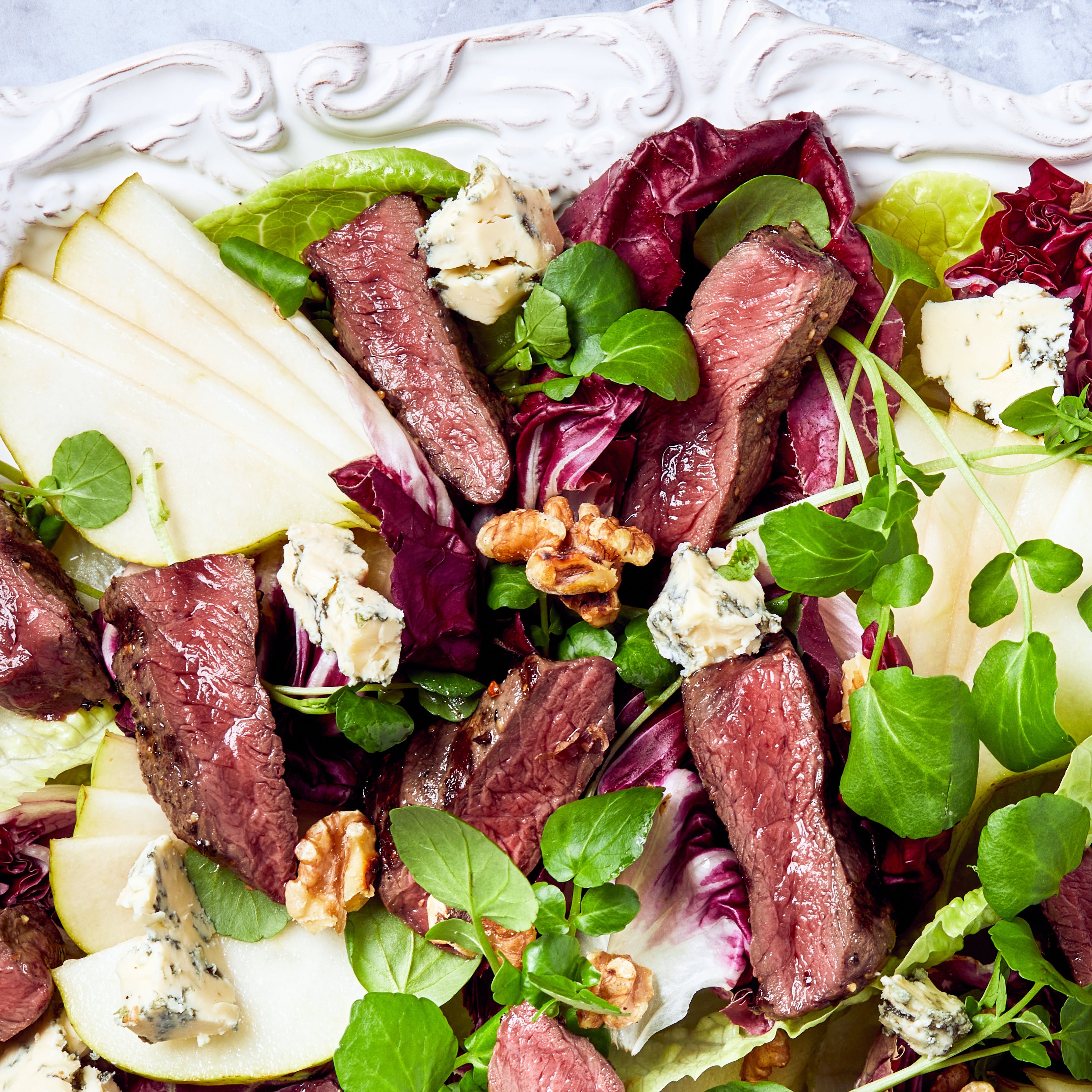 Salad with beef, pears, and greens on a decorative plate