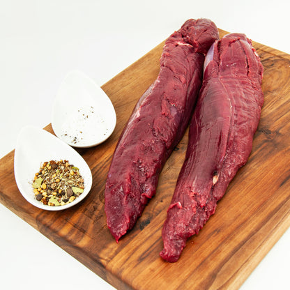 Two raw beef steaks on a wooden cutting board with seasonings.