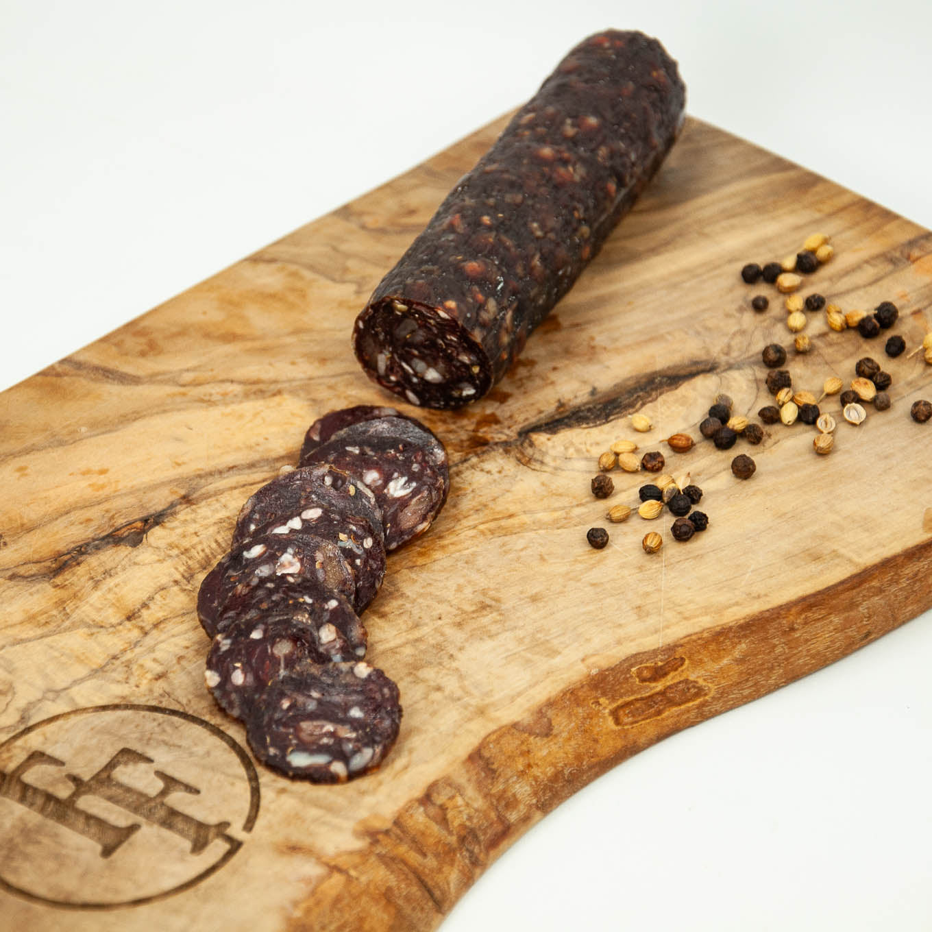 Rolled sausage with slices on a wooden cutting board with peppercorns