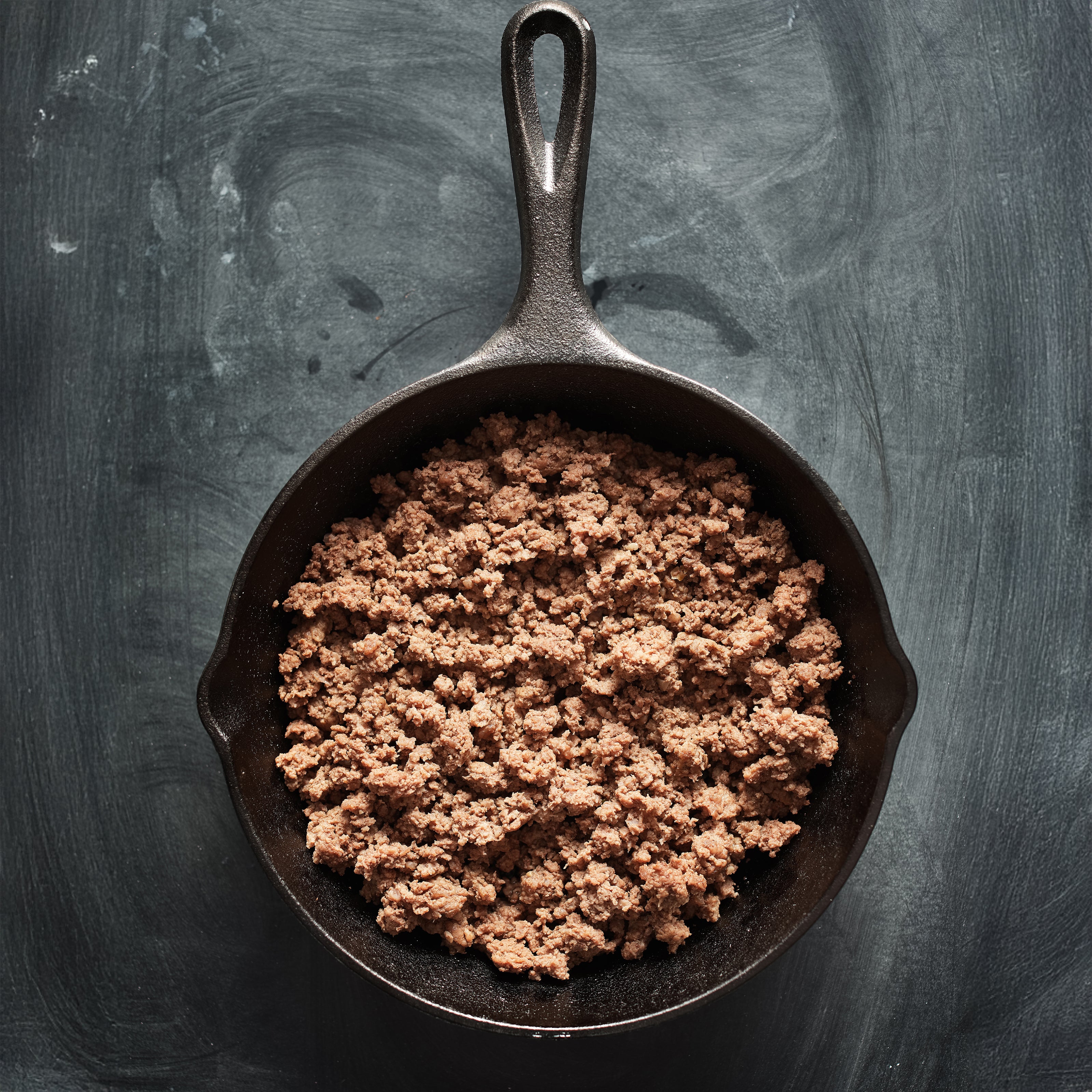 Browned ground meat in a cast iron skillet on a dark background