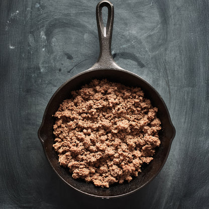 Browned ground meat in a cast iron skillet on a dark background