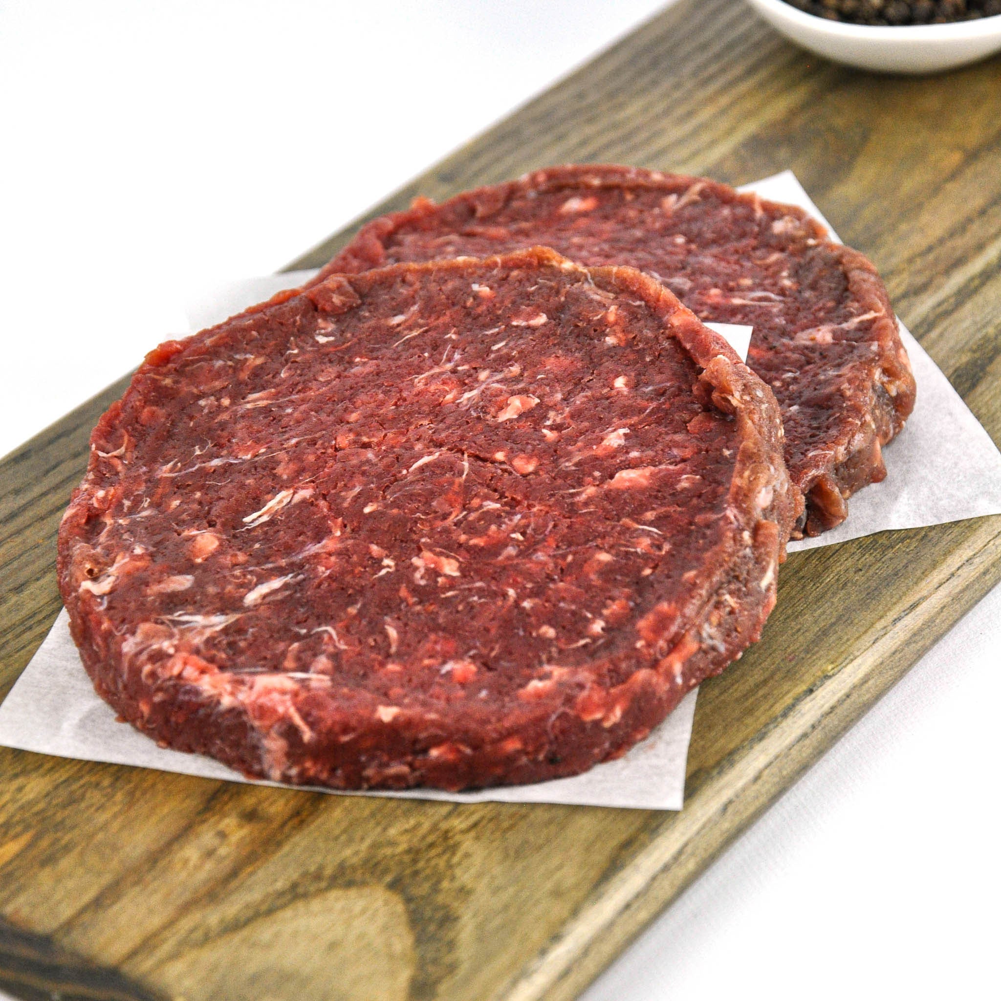 Two raw hamburger patties on a wooden cutting board with a white background