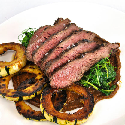 Sliced steak with grilled vegetables on a white plate