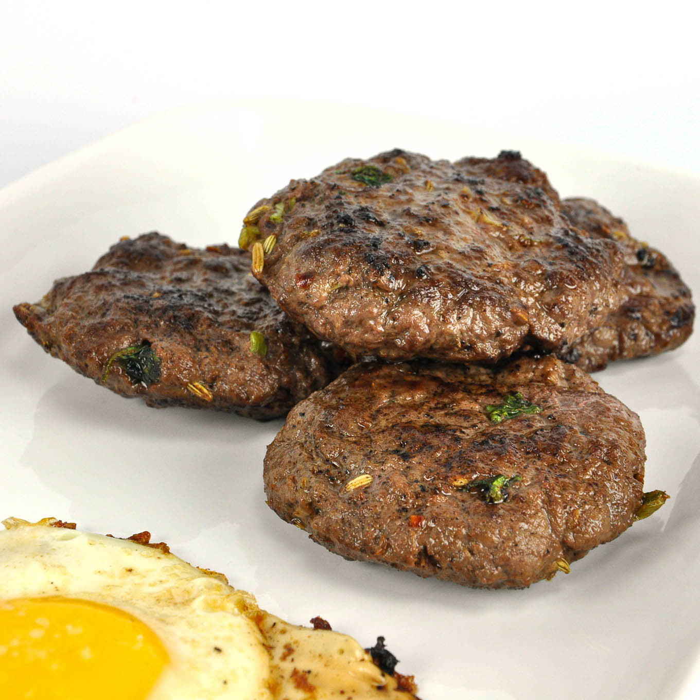 Three grilled hamburger patties on a white plate with a side of sunny-side-up eggs.