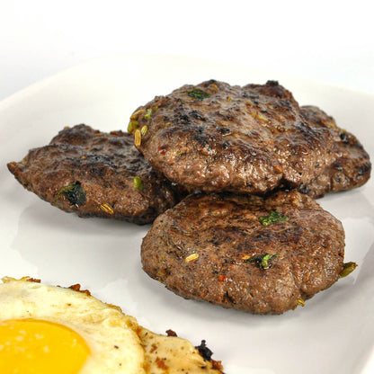 Three grilled hamburger patties on a white plate with a side of sunny-side-up eggs.