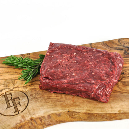 Raw beef on a wooden cutting board with rosemary, featuring a brand logo.