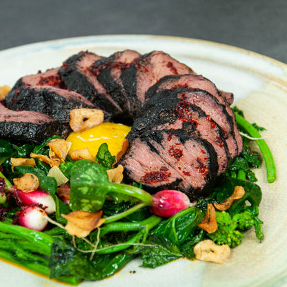Sliced roasted beef with green vegetables on a white plate