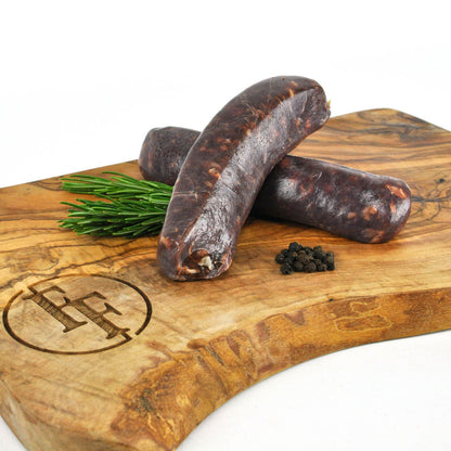 Three dried sausages on a wooden cutting board with rosemary and peppercorns.