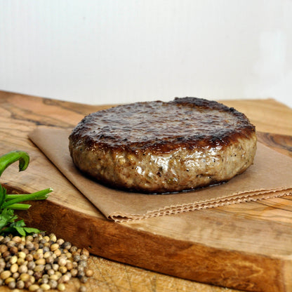Grilled hamburger patty on a wooden cutting board with herbs and spices.