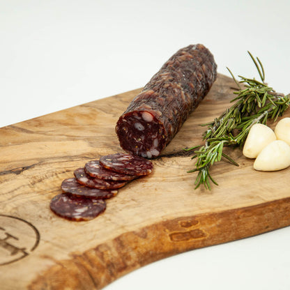 Rolled salami with slices on a wooden board with rosemary and garlic.