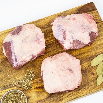 Three raw meat portions on a wooden cutting board with herbs and spices.