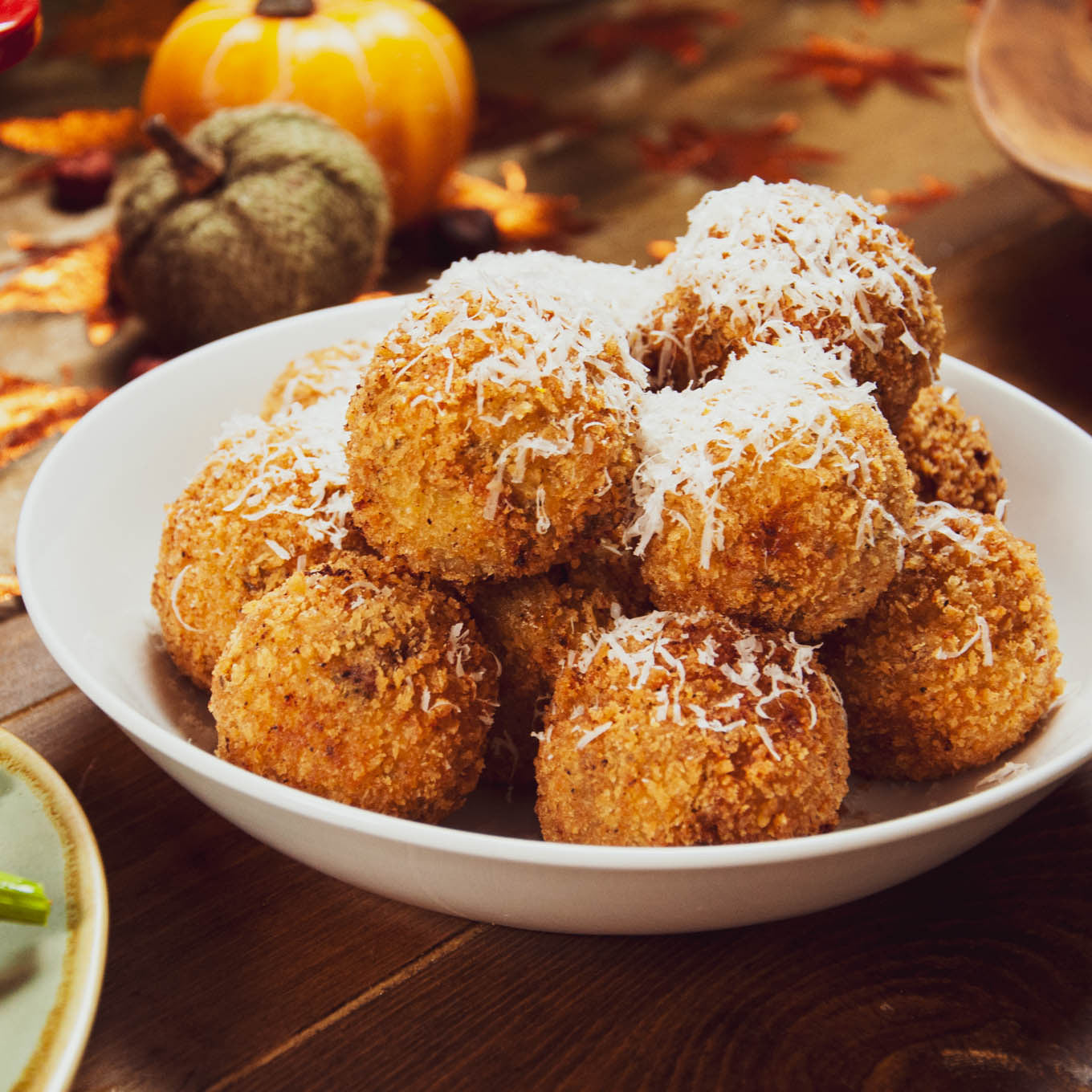 Bowl of fried balls with coconut on a wooden table with pumpkins and leaves.