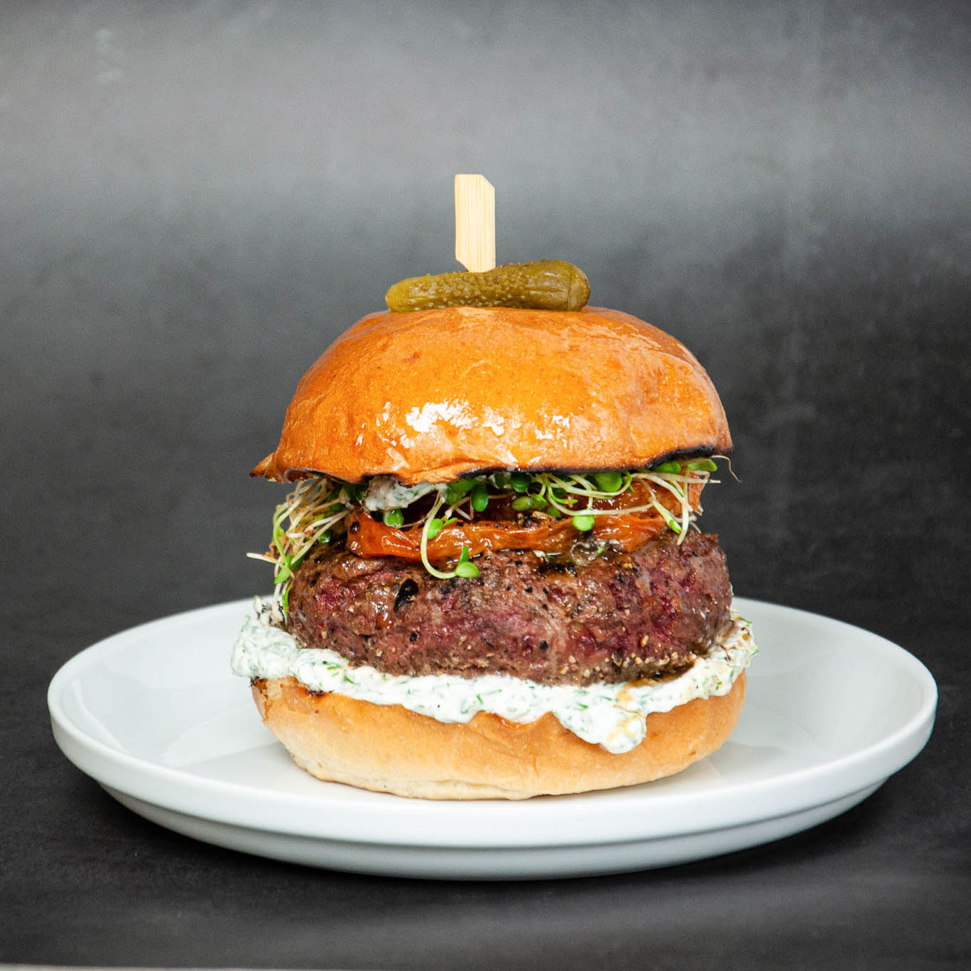 Hamburger with a pickle on top, served on a white plate against a dark background