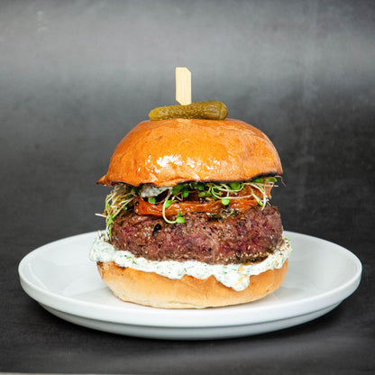 Hamburger with a pickle on top, served on a white plate against a dark background