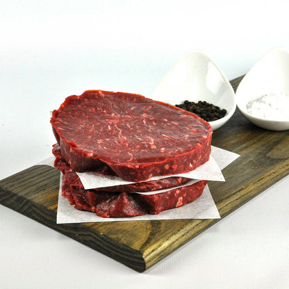 Raw beef steaks on a wooden cutting board with salt and pepper shakers.