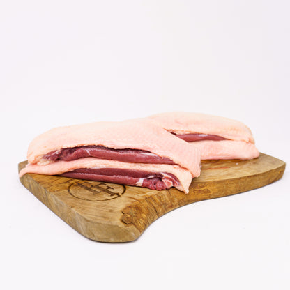 Raw duck breasts on a wooden cutting board with a white background