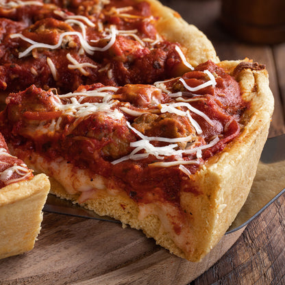 Close-up of a deep-dish pizza with a slice cut out on a wooden board.