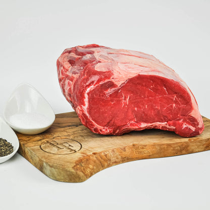 Raw steak on a wooden cutting board with salt and pepper shakers on a white background