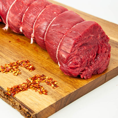 Rolled raw meat on a wooden cutting board with red pepper flakes.