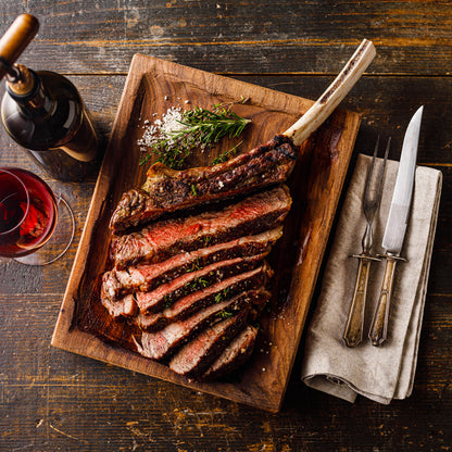 Sliced steak on a wooden platter with a bottle of wine and glasses on a rustic wooden table.