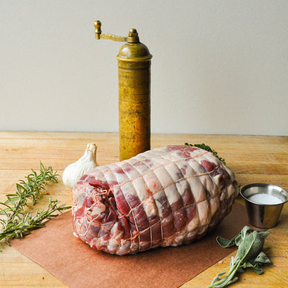 Raw meatloaf on a wooden board with herbs, garlic, and a pepper grinder.