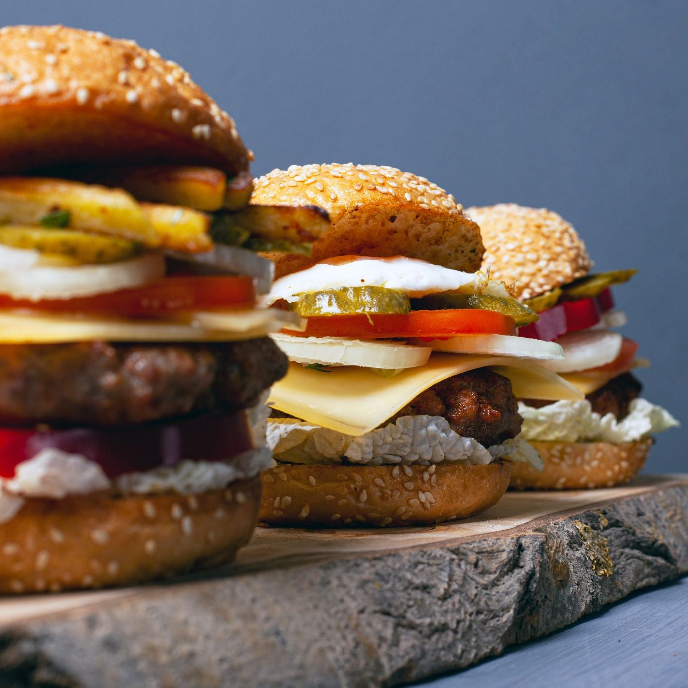 Three burgers with various ingredients on a wooden board against a blue background